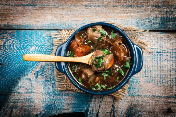 Meat stew with vegetables and herbs on old wooden table